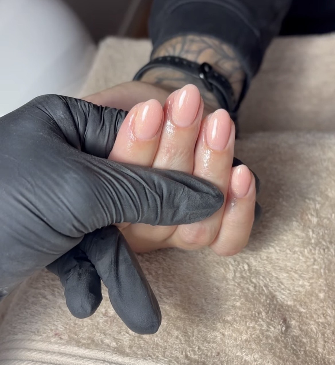 Een hand met naturel BIAB nagels, vastgehouden met een zwarte handschoen